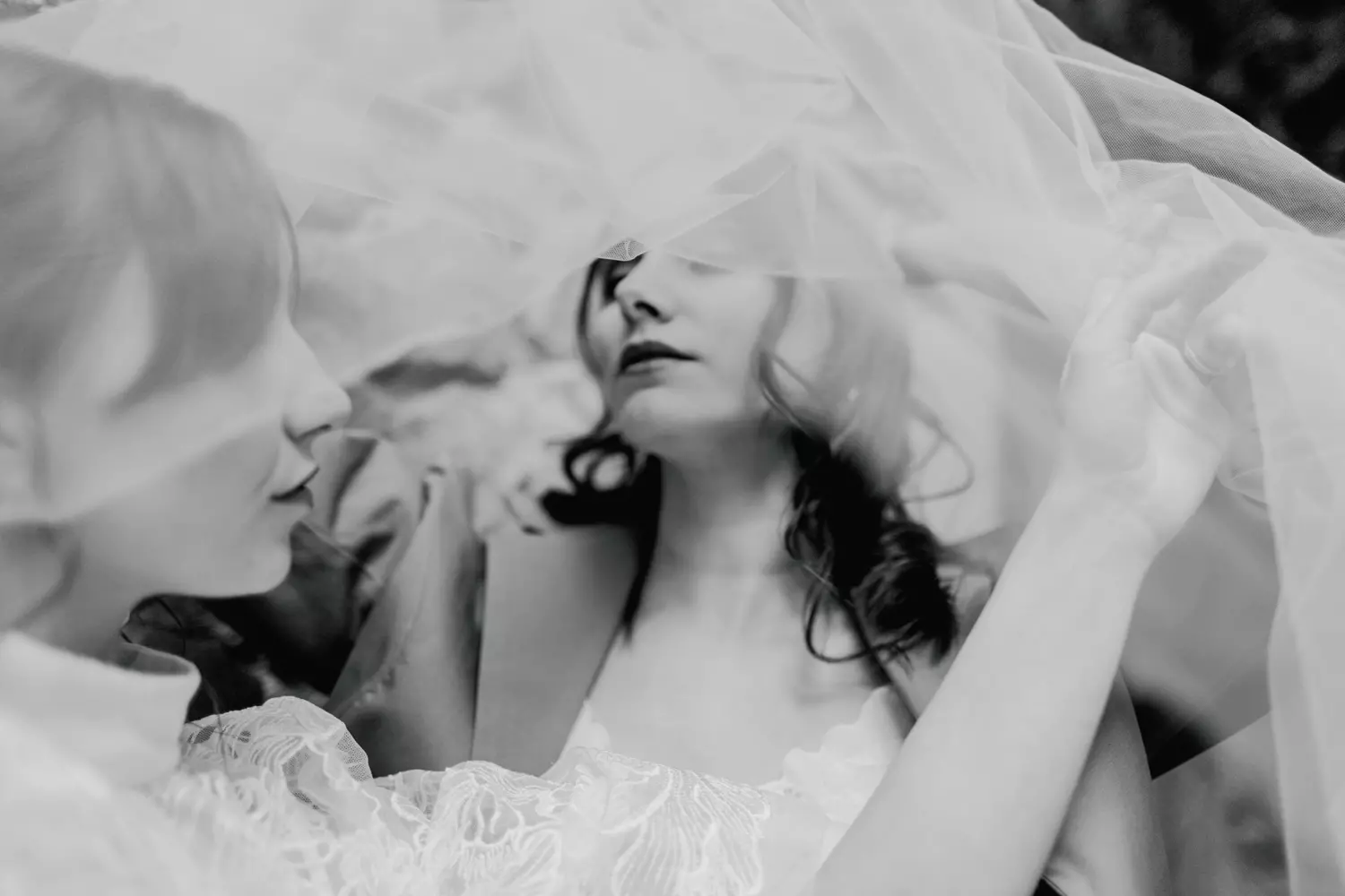 Photographie en noir et blanc sous le voile d'une des mariées mais toute deux sont dessous.