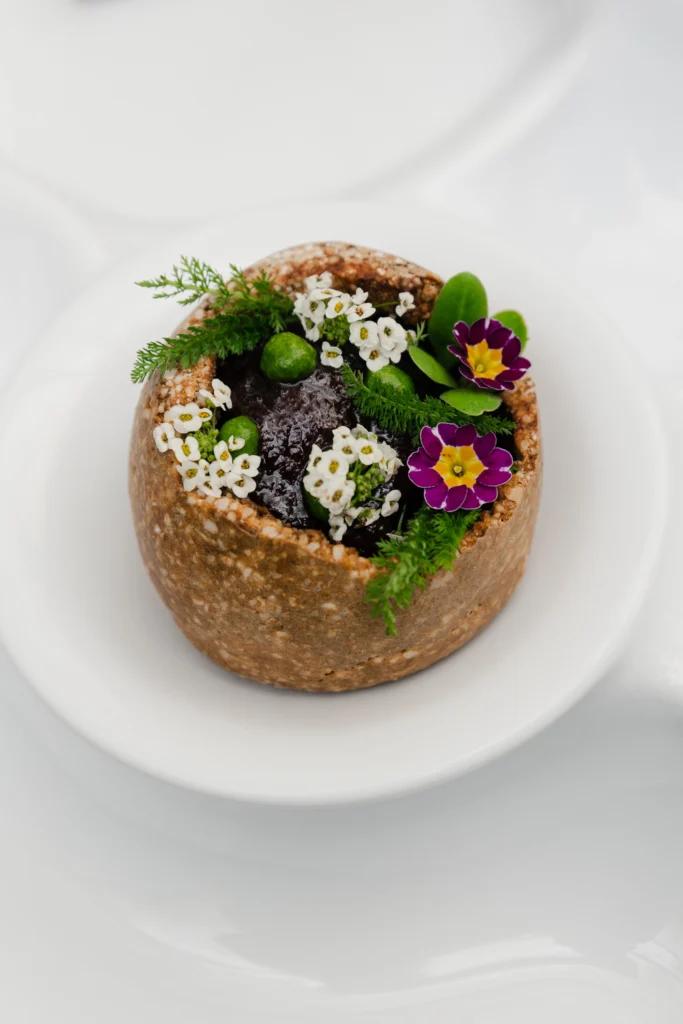 une photographie en portrait où on aperçoit uniquement le produit, croute de sel où à l'intérieur il y a de la betterave cuite, agrémenter de fleurs comestibles sur une assiette blanche.