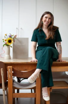 Portait d'une femme, se tenant assise sur une table. Dessus est posé un bouquet de fleurs et un album photo de mariage.