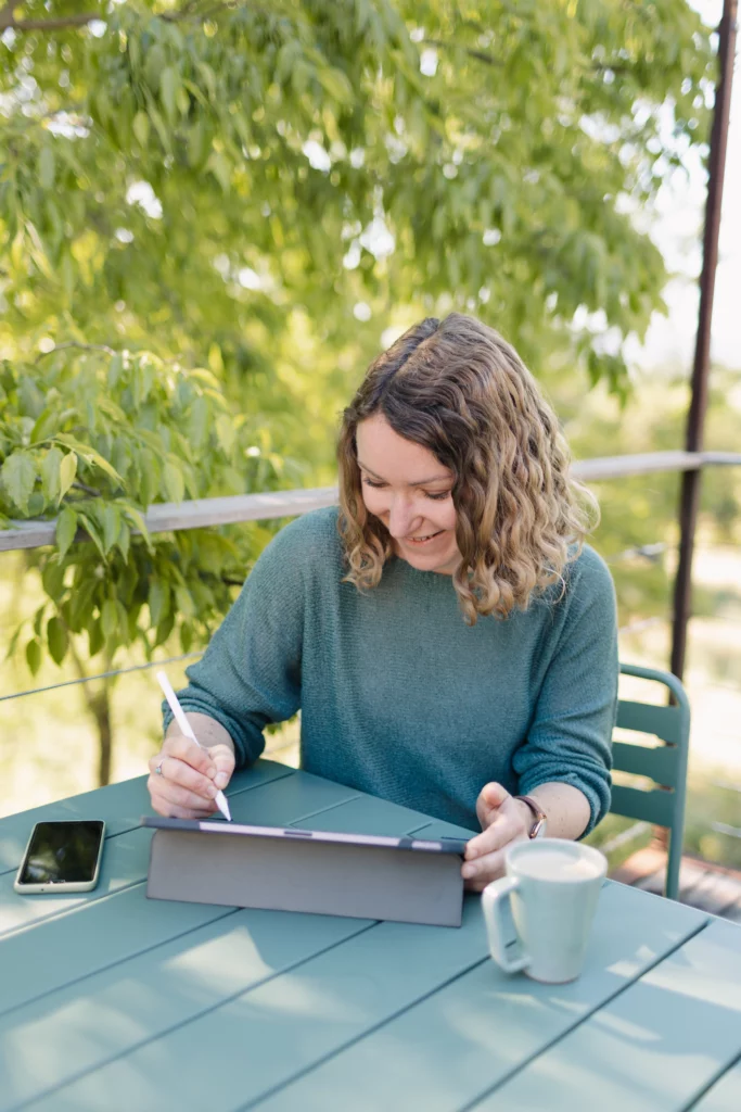 Une femme est assise en extérieur, elle est penché sur sa tablette graphique et tenant dans sa main un stylet.