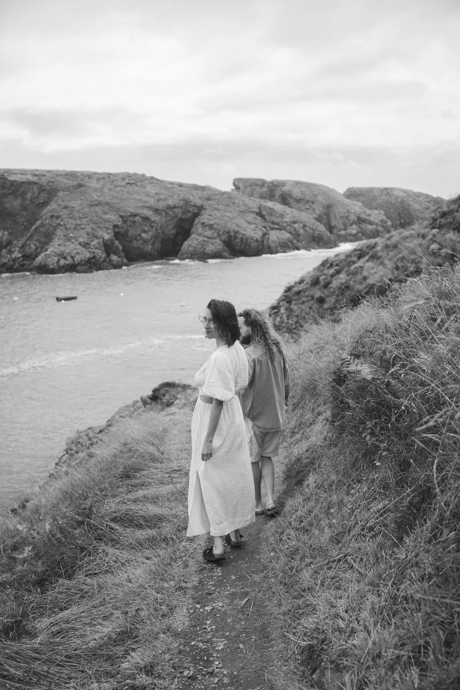 Au bord de mer, le long d'un chemin un couple marche main dans la main et où la femme se retourne vers moi.