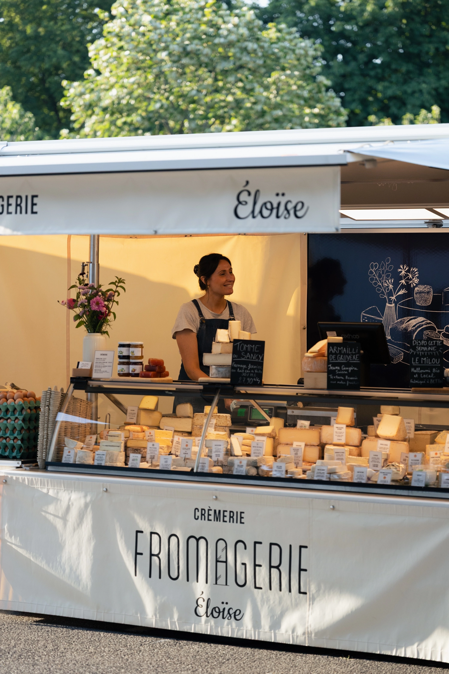 Une femme se tient derrière son comptoir, une fromagerie.