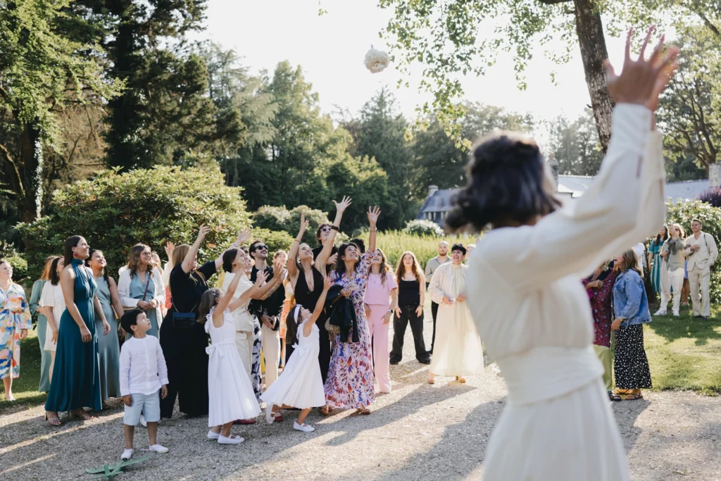 Une femme en robe blanche lance un bouquet et au second plan des femmes les mains prêtes à attraper le bouquet.