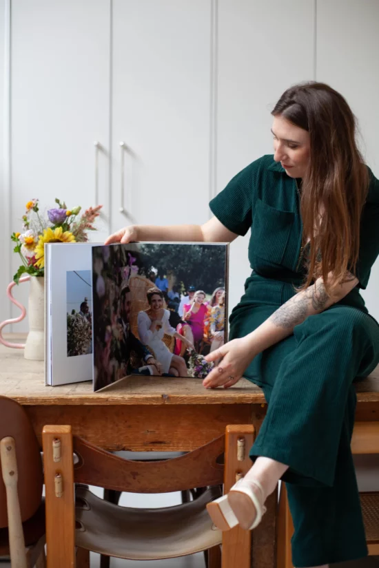 Une femme assise sur une table, tourne les pages d'un album photo de mariage.