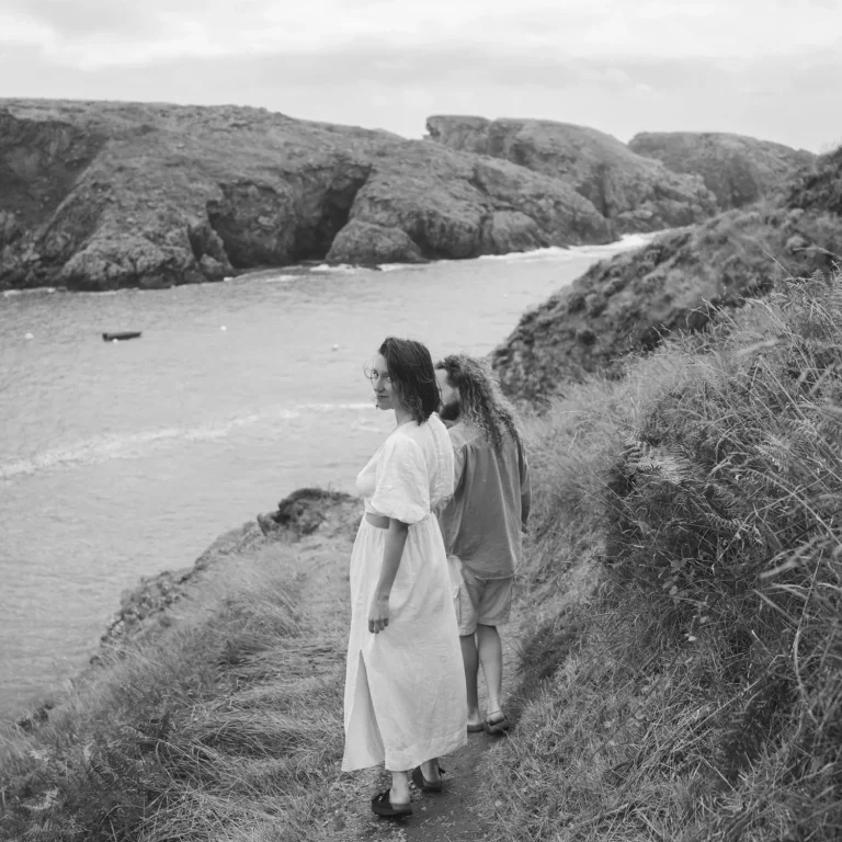 Au bord de mer, le long d'un chemin un couple marche main dans la main et où la femme se retourne vers moi.