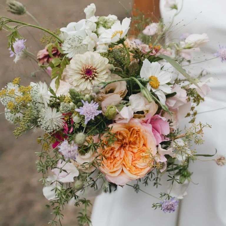 gros plan sur une jeune mariée tenant un bouquet de fleurs aux couleurs pastel.