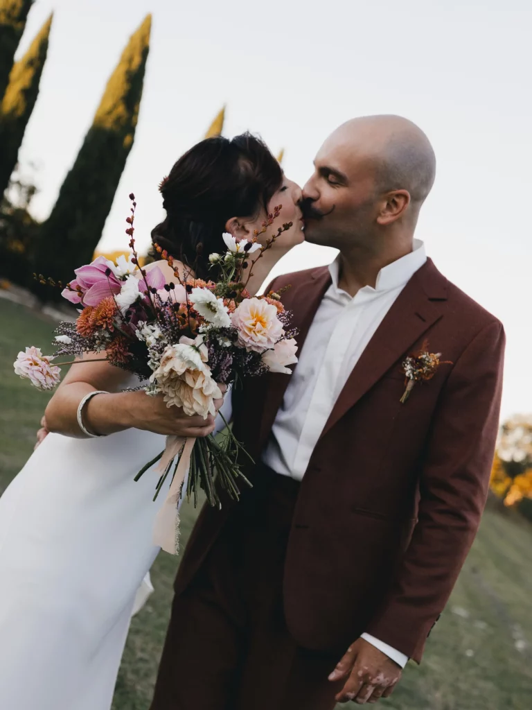 domethilde_photographe_mariage_bretagne_couple Un couple s'embrasse, la femme tenant un bouquet dans ses mains, tandis que l'homme enlace sa femme.